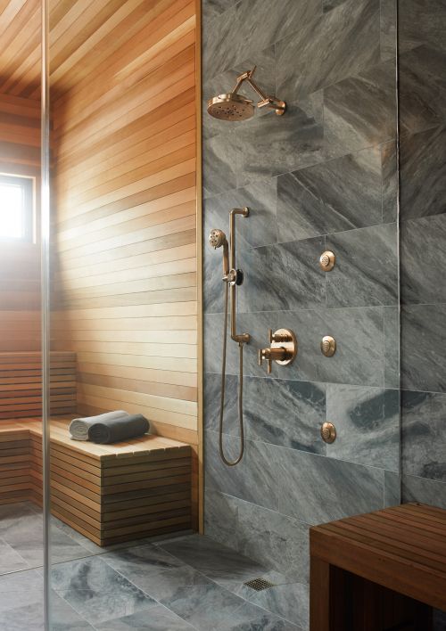 Modern bathroom interior with a wood sauna bench, gray marble walls, rose gold shower fixtures, and a gray towel.