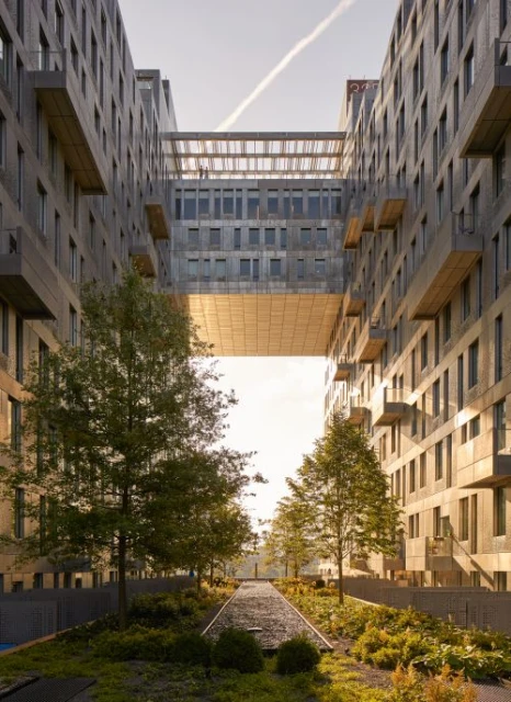 Exterior view of a modern residential building with a skybridge connecting two sections, surrounded by trees and greenery.