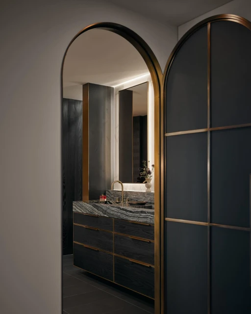 Modern bathroom interior featuring a vanity with a stone countertop, black cabinets, and a gold faucet, viewed through arched doorways.