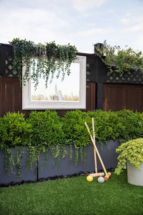 Croquet set and greenery in an outdoor setting with a framed mirror reflecting a cityscape, evokes a blend of nature and urbanity.