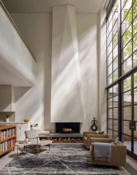 Spacious modern double height living room with a tall sculptural white fireplace, large floor to ceiling windows, and patterned rug.