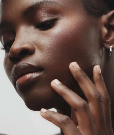 Close-up studio shot of Black woman touching her face. Beauty portrait features skin detail, minimal makeup, silver hoop earrings.