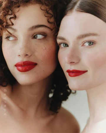 Close-up beauty portrait of two female models with vibrant red lipstick against a plain light background
