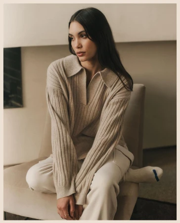 Woman in beige ribbed polo sweater seated on an armchair in a neutral interior