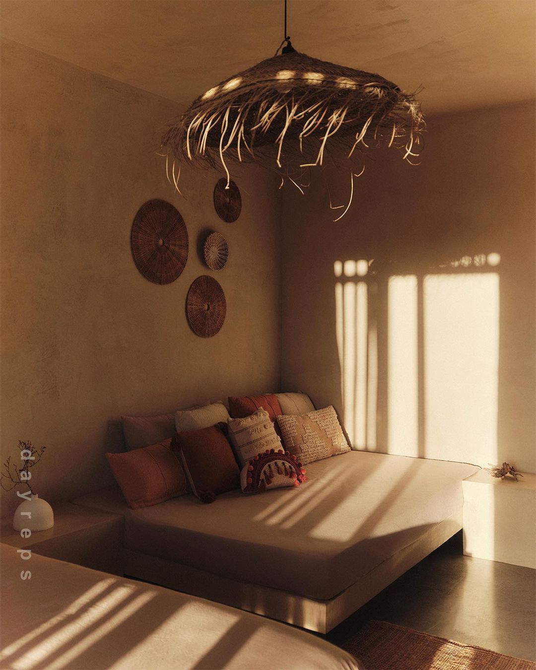 Bedroom interior with straw pendant light, platform bed with cushions, and wall decor with warm, inviting natural light.