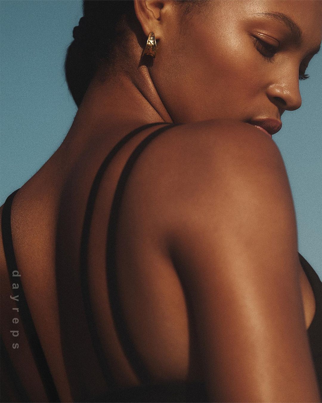 Close-up profile of a black woman wearing gold hoop earrings against a clear blue sky background