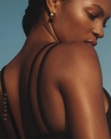 Close-up profile of a black woman wearing gold hoop earrings against a clear blue sky background
