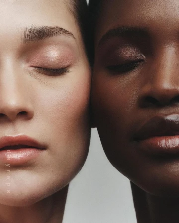 Close-up portrait of two female models with eyes closed pressing their faces together against a neutral background