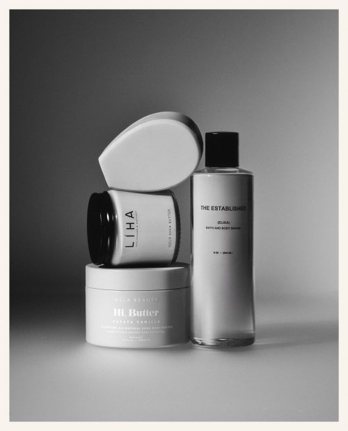 Black and white still life of beauty products stacked on top of each other, including lotions, oils, and scrubs for skincare.