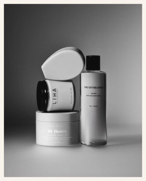 Black and white still life of beauty products stacked on top of each other, including lotions, oils, and scrubs for skincare.