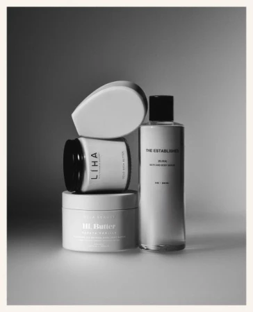 Black and white still life of beauty products stacked on top of each other, including lotions, oils, and scrubs for skincare.