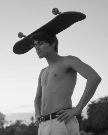 Shirtless young man balancing a skateboard on his head against an outdoor sky background, photographed by Wolfe + Von.