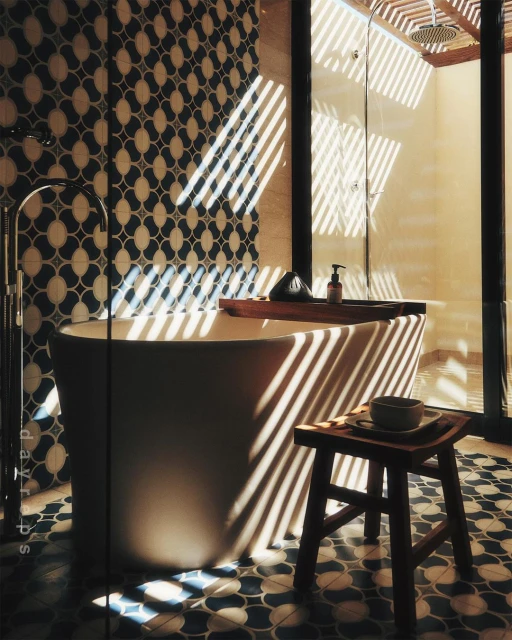 Freestanding bathtub in a modern bathroom with patterned tile and natural sunlight streaming through louvered window coverings.