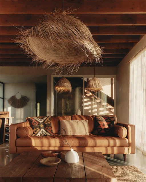 Living room interior features a brown leather sofa with patterned cushions, a wooden coffee table, straw light fixtures, and natural light.