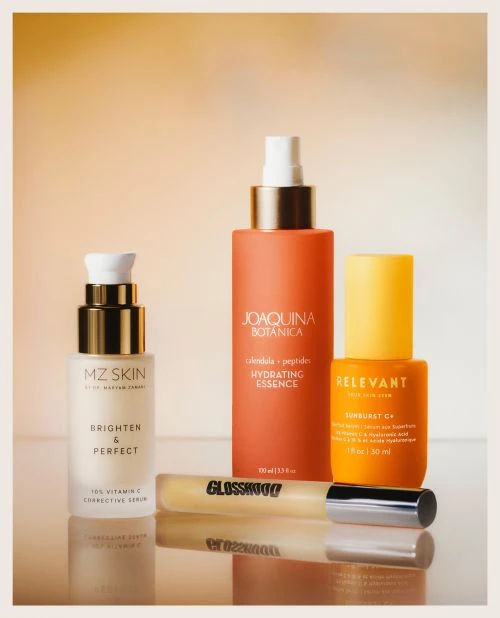 A collection of skin care products including serums, lotions, and lip gloss, arranged against a soft orange background in a studio setting.