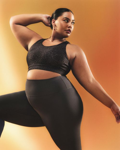 Adult female in workout attire posing confidently against a warm orange background, highlighting fitness and active lifestyle.
