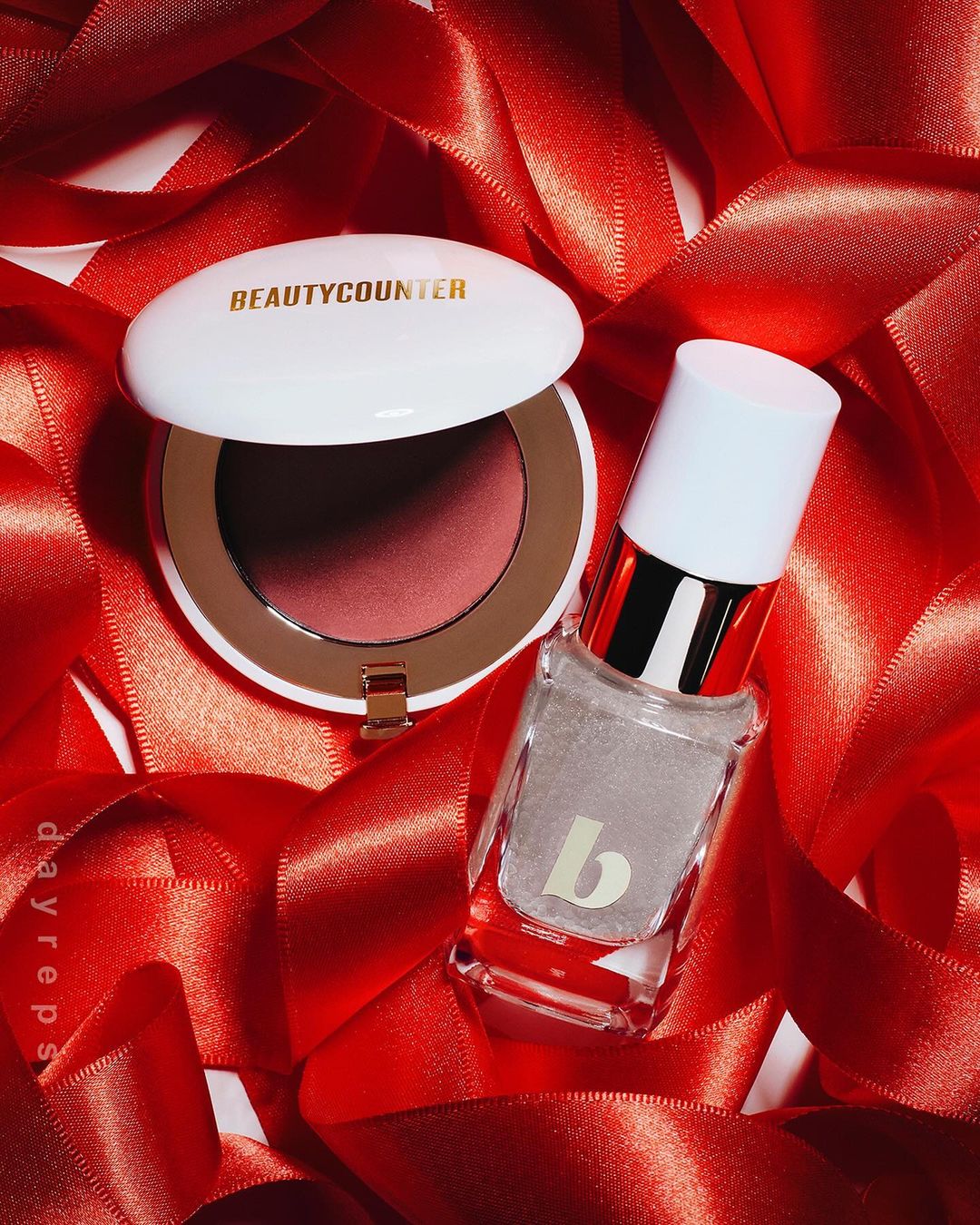 BeautyCounter blush and nail polish displayed on red satin ribbon. Cosmetic products for makeup and beauty on elegant backdrop.