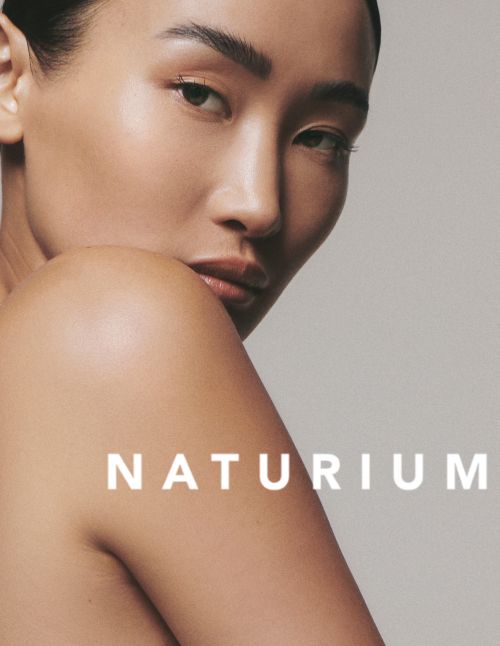 Close-up studio shot of an adult Asian woman with glowing skin, minimal makeup, and visible brand text "NATURIUM."