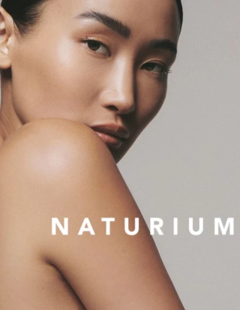Close-up studio shot of an adult Asian woman with glowing skin, minimal makeup, and visible brand text "NATURIUM."