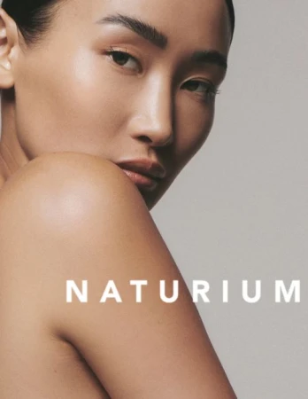 Close-up studio shot of an adult Asian woman with glowing skin, minimal makeup, and visible brand text "NATURIUM."