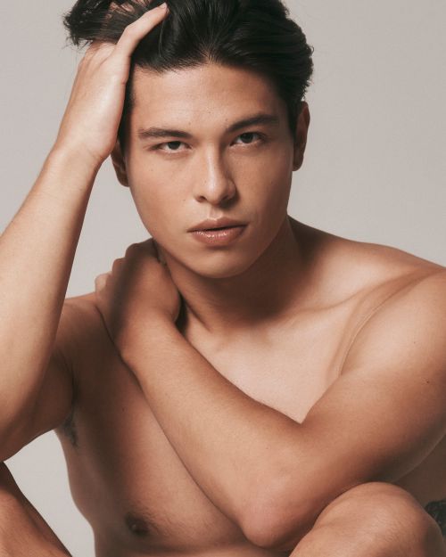 Portrait of a shirtless adult male with dark hair, looking at the camera, set against a neutral background in a close-up studio shot.