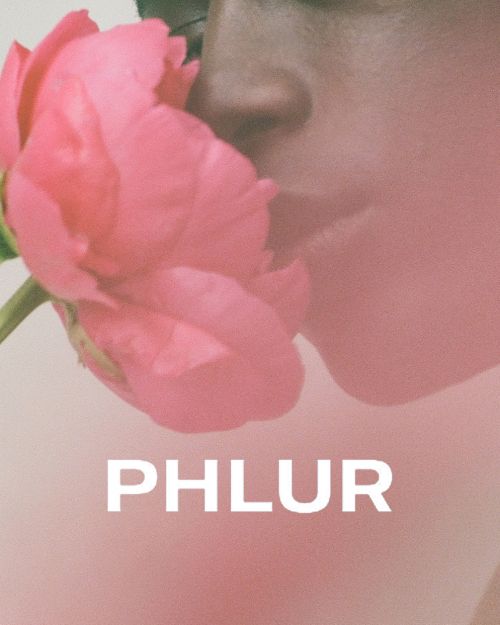 Close-up of an adult with a pink flower near their face, soft pink background, and the text "PHLUR" in white, minimal aesthetic.