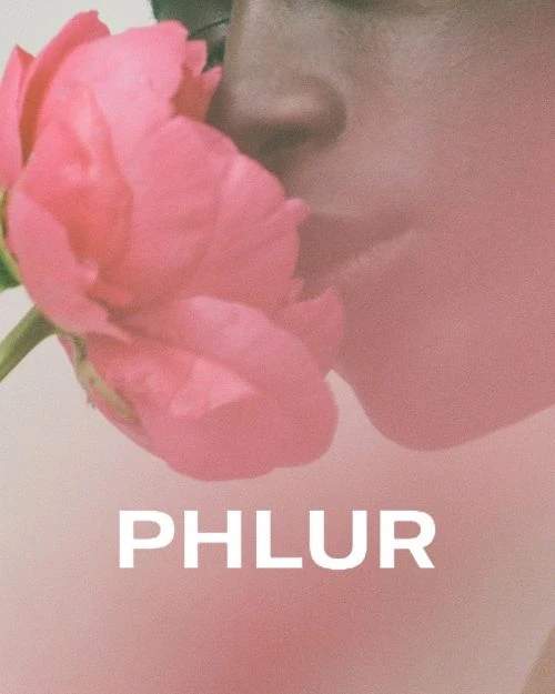 Close-up of an adult with a pink flower near their face, soft pink background, and the text "PHLUR" in white, minimal aesthetic.