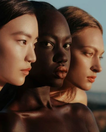 Close-up portrait of three female models with diverse ethnicities in warm golden hour sunlight.