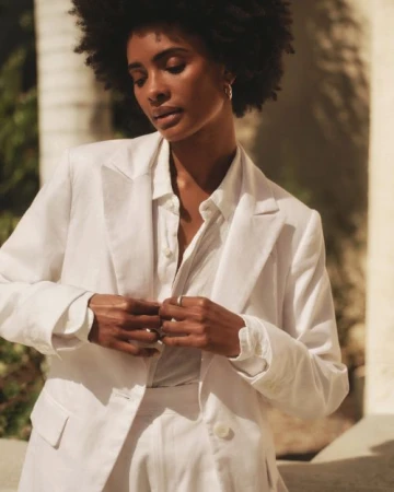 Black woman with afro hairstyle wearing a white blazer and button-down shirt outdoors in warm sunlight.