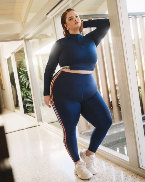 A woman in a navy blue athletic set poses in front of a set of glass doors in a brightly lit, indoor setting.