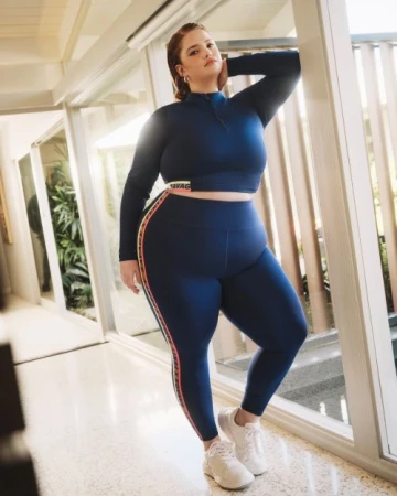 A woman in a navy blue athletic set poses in front of a set of glass doors in a brightly lit, indoor setting.