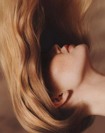 Close-up profile of a woman with long blonde hair and freckles in soft warm lighting by Wolfe + Von