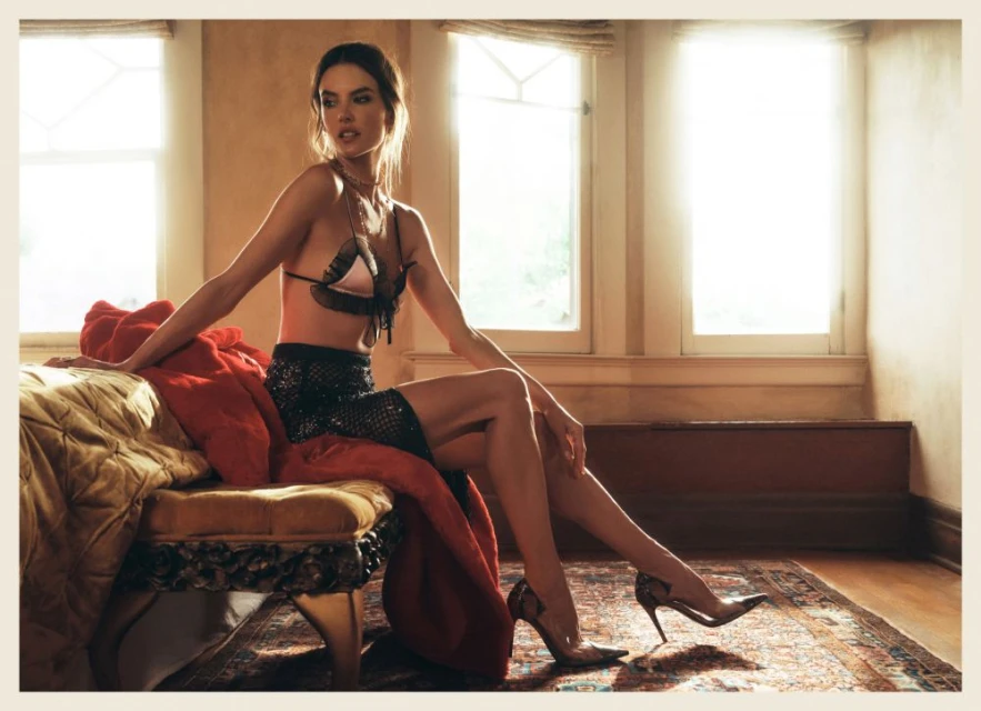 Elegant woman in bra and skirt posing on bench in naturally lit room.  Bedroom fashion shot with soft colors and window light.