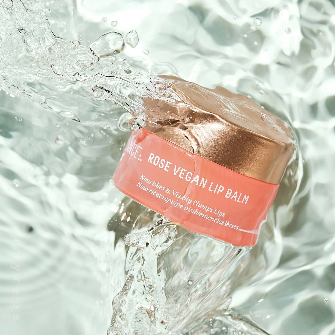 Rose vegan lip balm jar splashing in water, surrounded by clear aqua liquid. Cosmetic product shot with simple watery background.