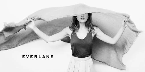 Woman in tank top holds up gray scarf against a white background in a studio shot featuring the Everlane logo.