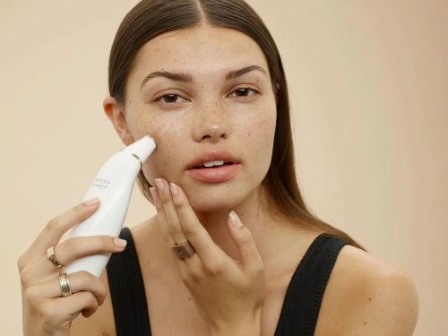 Adult female using white beauty device on her face in an indoor setting with a neutral background. Close-up product shot.