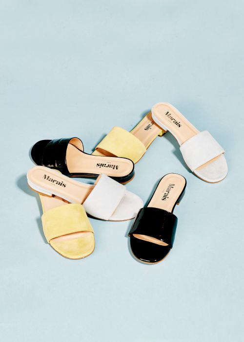 Group of women's slide sandals in yellow, white and black leather on a light blue surface. Fashion footwear editorial product shot.