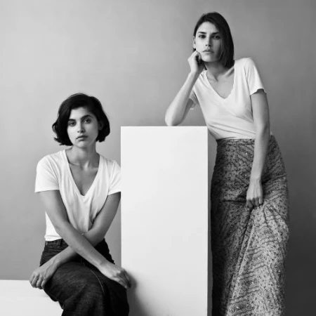 Two women posing in black and white with a white rectangular prop in a minimalist studio setting.