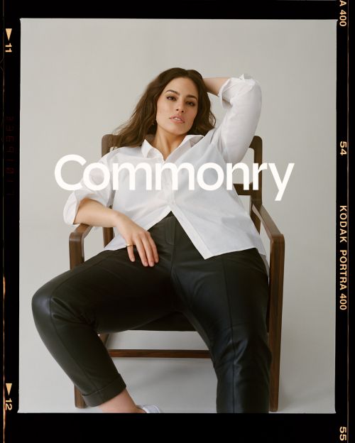 Woman in white shirt and black pants sits in wooden chair against neutral backdrop, promoting the Commonry brand, in a fashion editorial setting.
