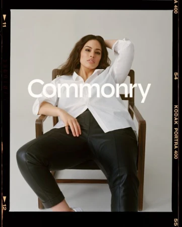 Woman in white shirt and black pants sits in wooden chair against neutral backdrop, promoting the Commonry brand, in a fashion editorial setting.