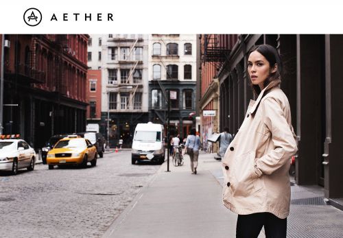 Woman wearing a beige trench coat standing on a cobblestone street with a yellow taxi in the background