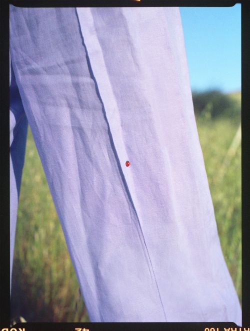 Close-up of a light purple shirt, emphasizing its texture and color, set against a blurred background of green grass and blue sky.
