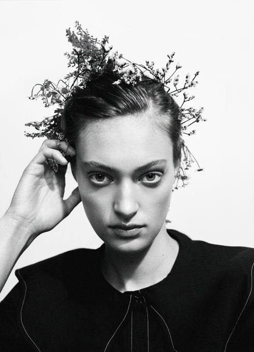 Monochrome portrait of a woman with floral headpiece against a white backdrop, in a beauty or fashion context, with studio lighting.