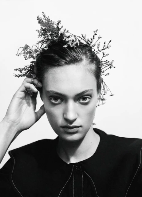 Monochrome portrait of a woman with floral headpiece against a white backdrop, in a beauty or fashion context, with studio lighting.
