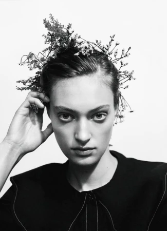 Monochrome portrait of a woman with floral headpiece against a white backdrop, in a beauty or fashion context, with studio lighting.