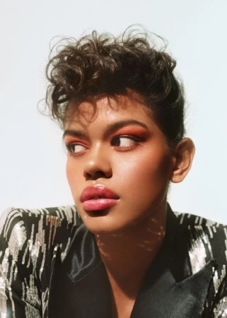 Portrait of a woman with curly hair wearing a patterned black jacket against a plain background