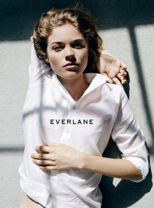 Blonde woman in a white shirt lying on a gray surface with a shadow, staring at the camera. Features the Everlane logo.