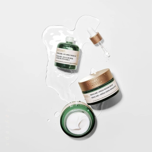 Overhead shot of Biossance Squalane + Vitamin C rose oil and Squalane + Omega repair cream in a minimalistic setting with water droplets.