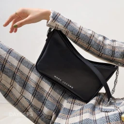 Close-up of a person wearing plaid trousers and a matching jacket, holding a black leather Marc Jacobs shoulder bag.