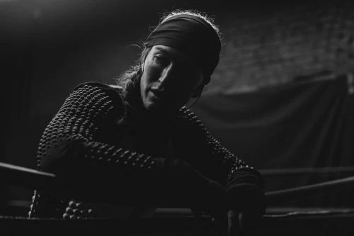 Monochrome portrait of an adult female athlete resting after workout in dark interior. Close-up shot with overhead lighting and textured top.